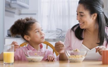 Mother and daughter (4-6) at table eating cereal